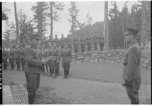Kenraaliluutnantti W.E.Tuompon 50-vuotispäivä. Rajavartiolaitoksen henkilökunnan lahjoittaman kesämajan luovutustilaisuudessa 24.9.1943 Pornaisissa. Eversti Villamo pitää luovutuspuhetta. Taustalla nähdään rakentajien ja lahjoittajien edustajat.